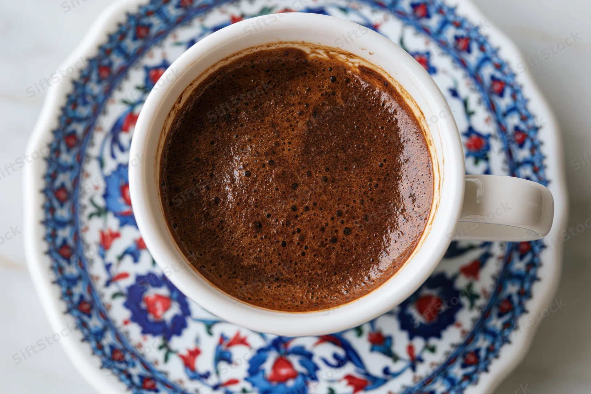Turkish coffee in a white ceramic cup with dense dark brown foam on a floral saucer viewed from above