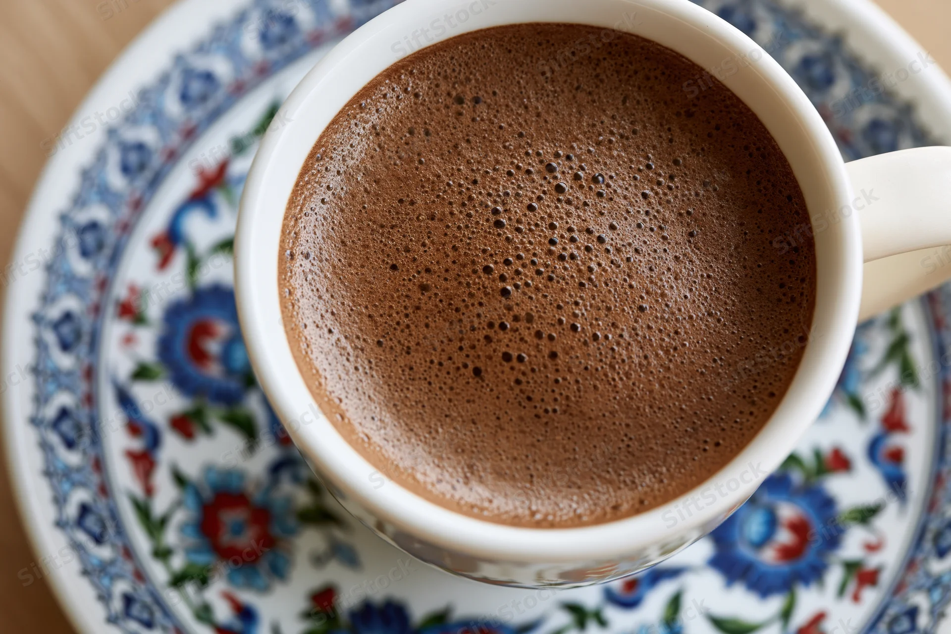 Turkish coffee with dense dark foam in a white ceramic cup on a floral saucer