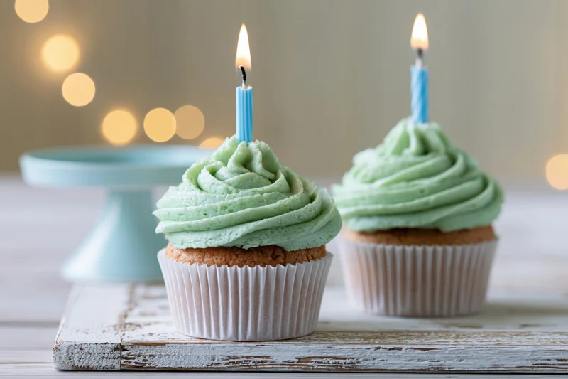 Two cupcakes with mint green frosting and lit candles on a rustic wooden board