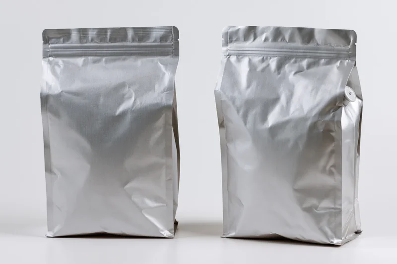 Two blank matte silver foil coffee bags standing upright side by side on white surface