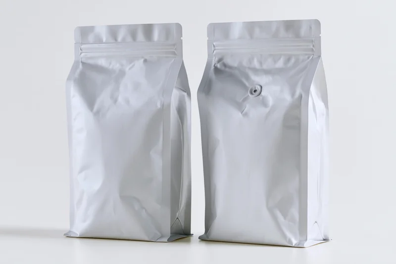 Two blank matte silver foil coffee bags standing upright side by side on white surface