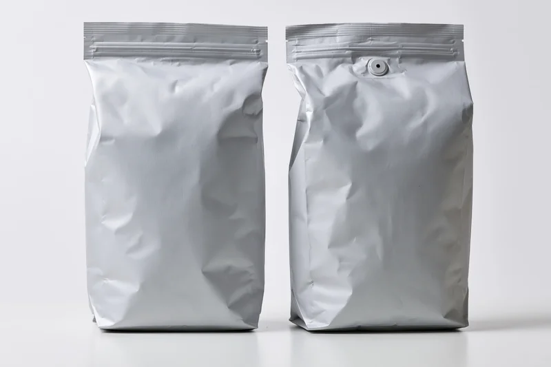 Two blank matte silver foil coffee bags standing upright side by side on white surface