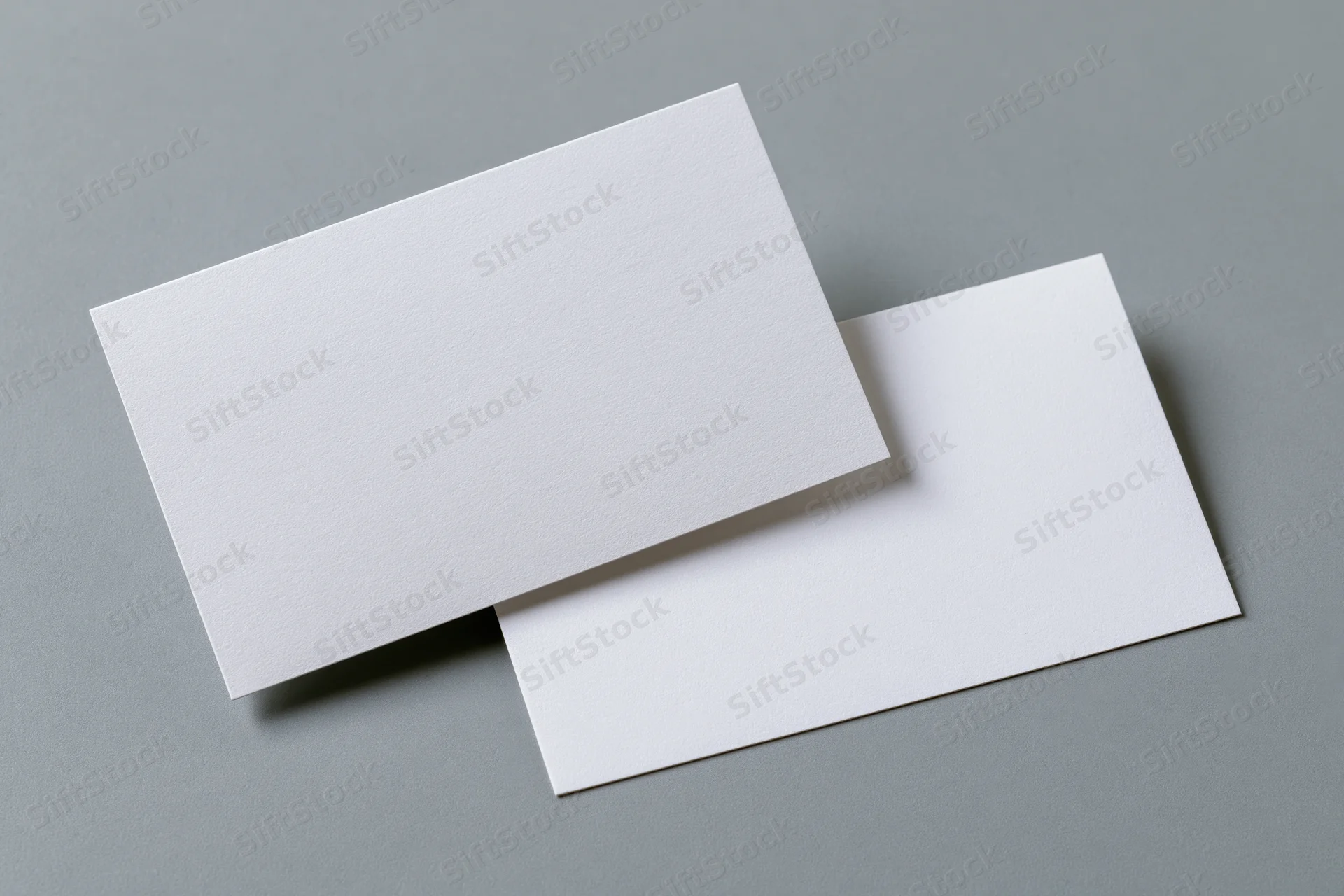 Two blank white business cards arranged at slight angles on a gray surface