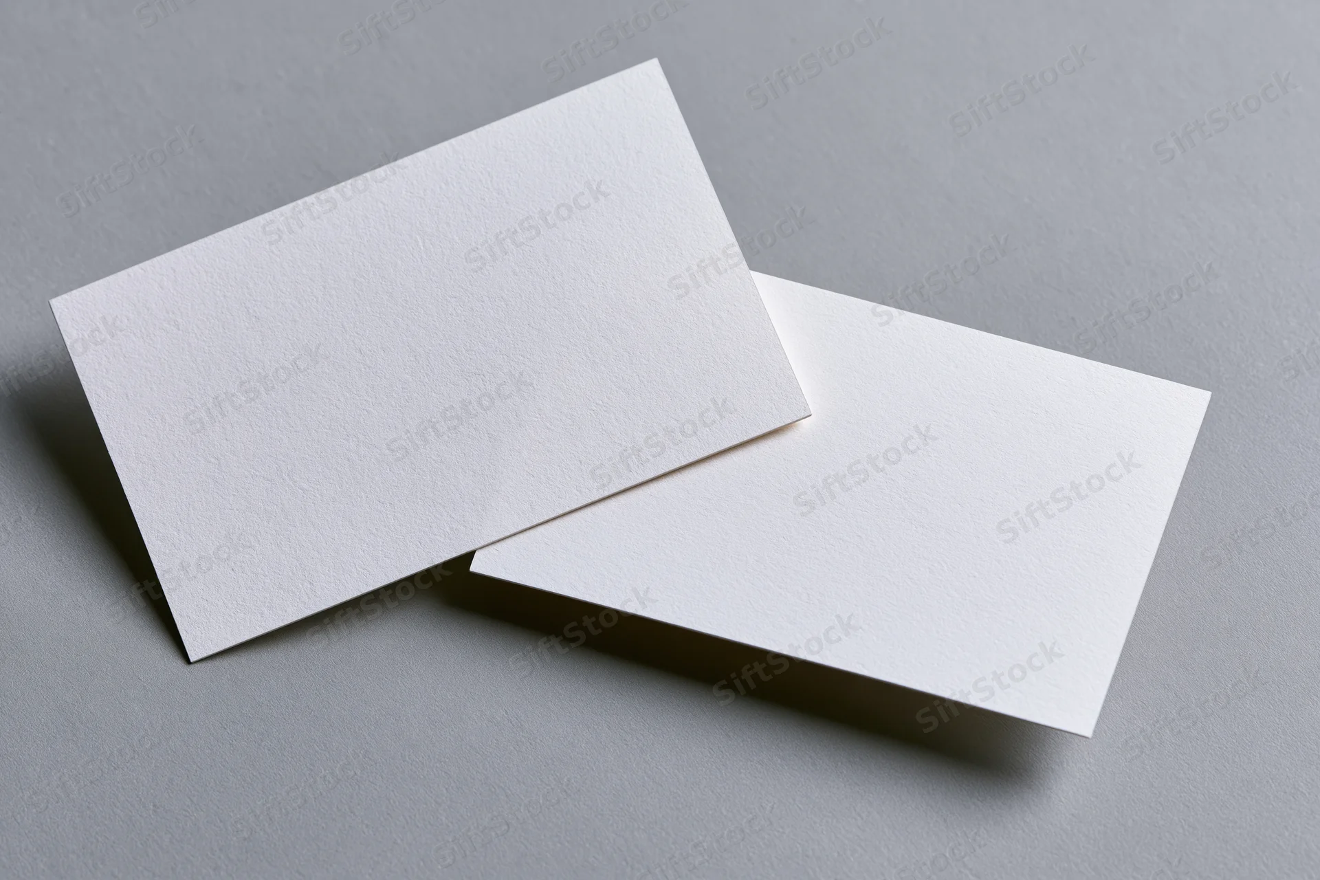Two blank white business cards arranged at slight angles on a gray surface