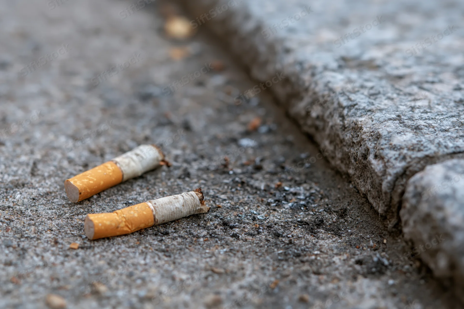 Two discarded cigarette butts on rough concrete pavement near a curb