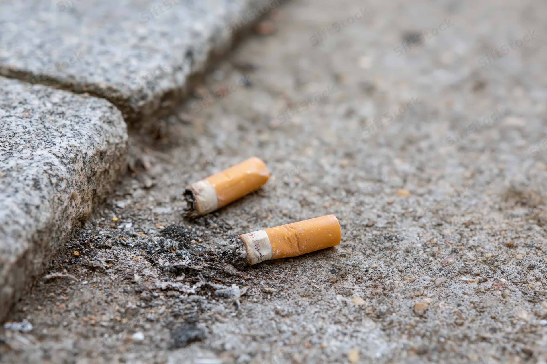 Two discarded cigarette butts lying on rough concrete pavement