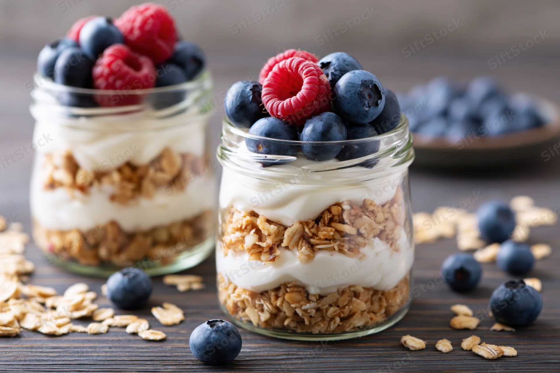 Two glass jars filled with layered granola, yogurt, and fresh berries on a dark wooden table