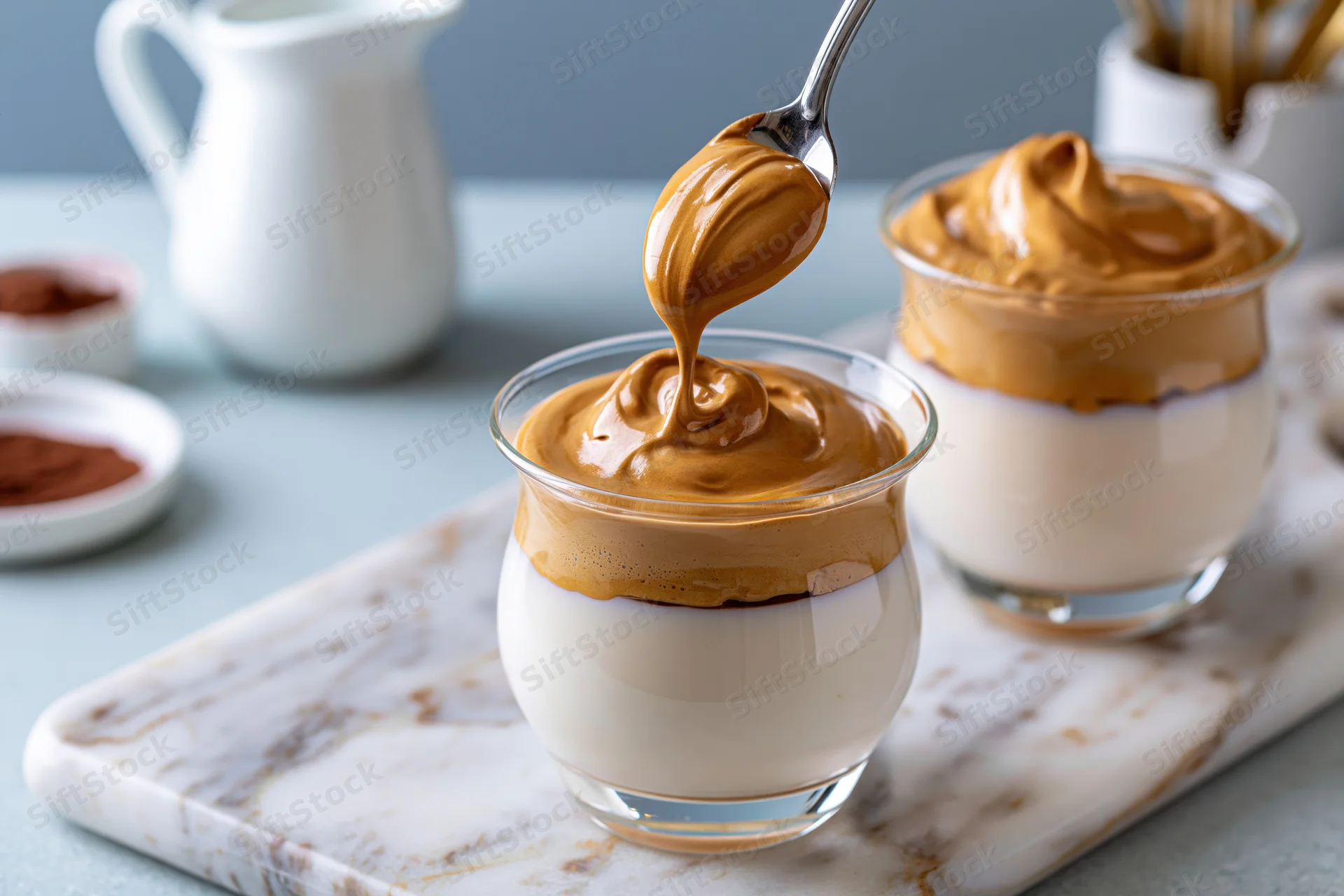 Spoon drizzling caramel topping onto dalgona whipped coffee in glass on marble board