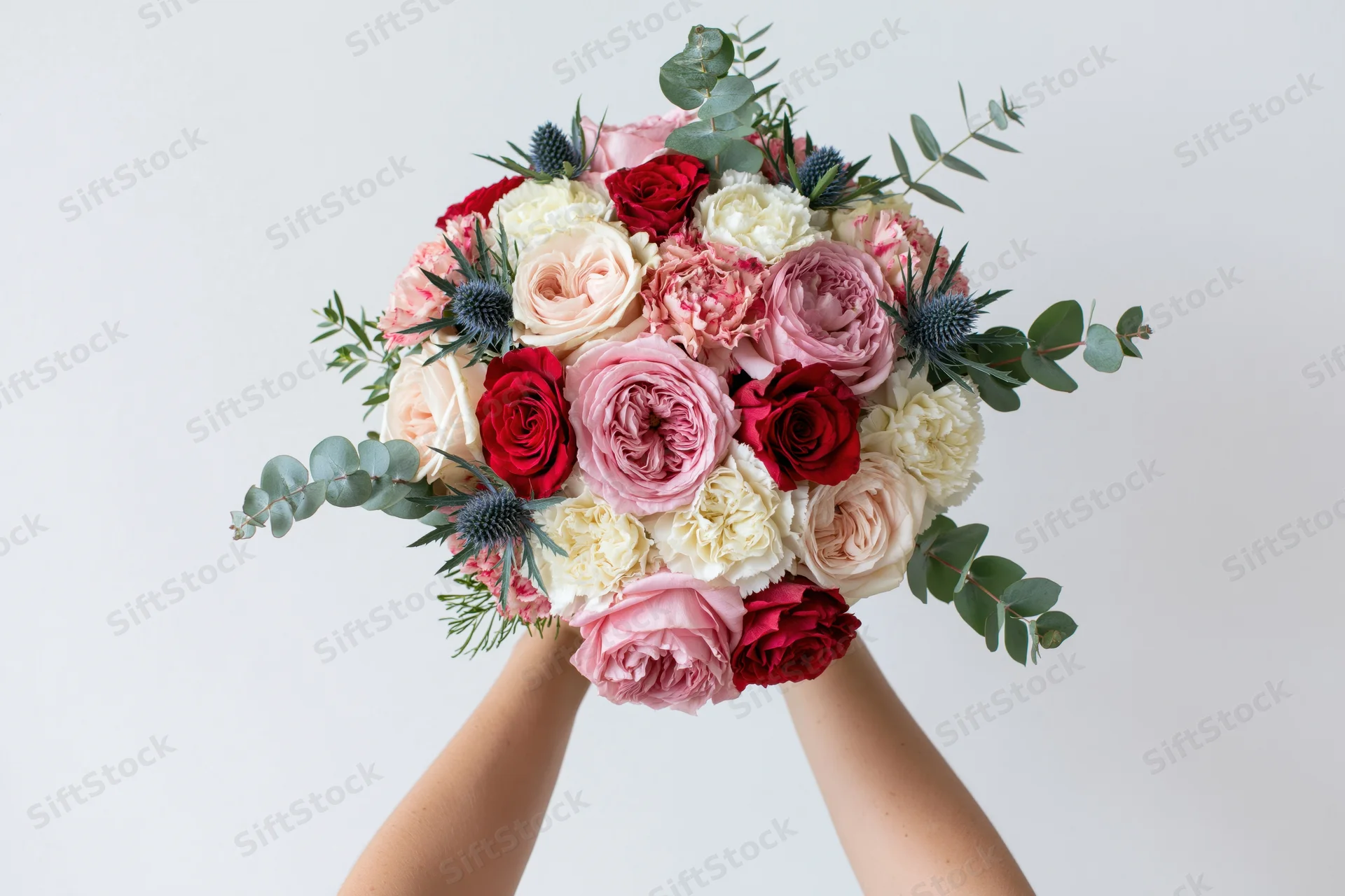 Hands holding a lush mixed flower bouquet against a plain white background