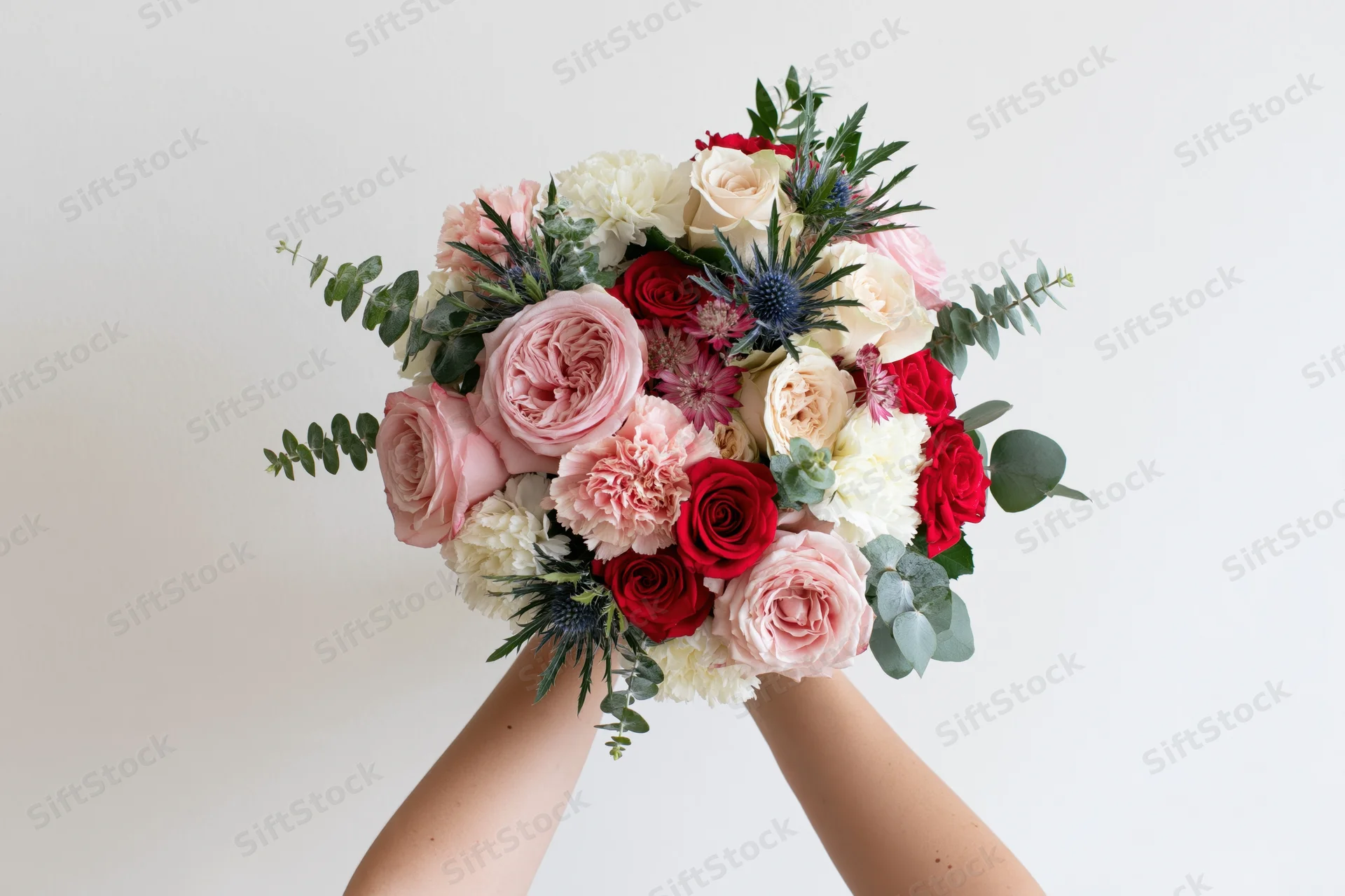 Hands holding a lush mixed flower bouquet against a plain white background