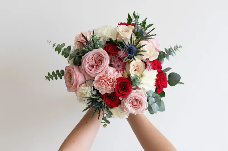 Hands holding a lush mixed flower bouquet against a plain white background