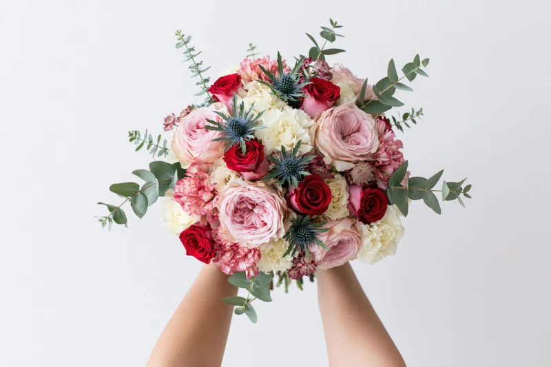 Hands holding a lush mixed flower bouquet against a plain white background