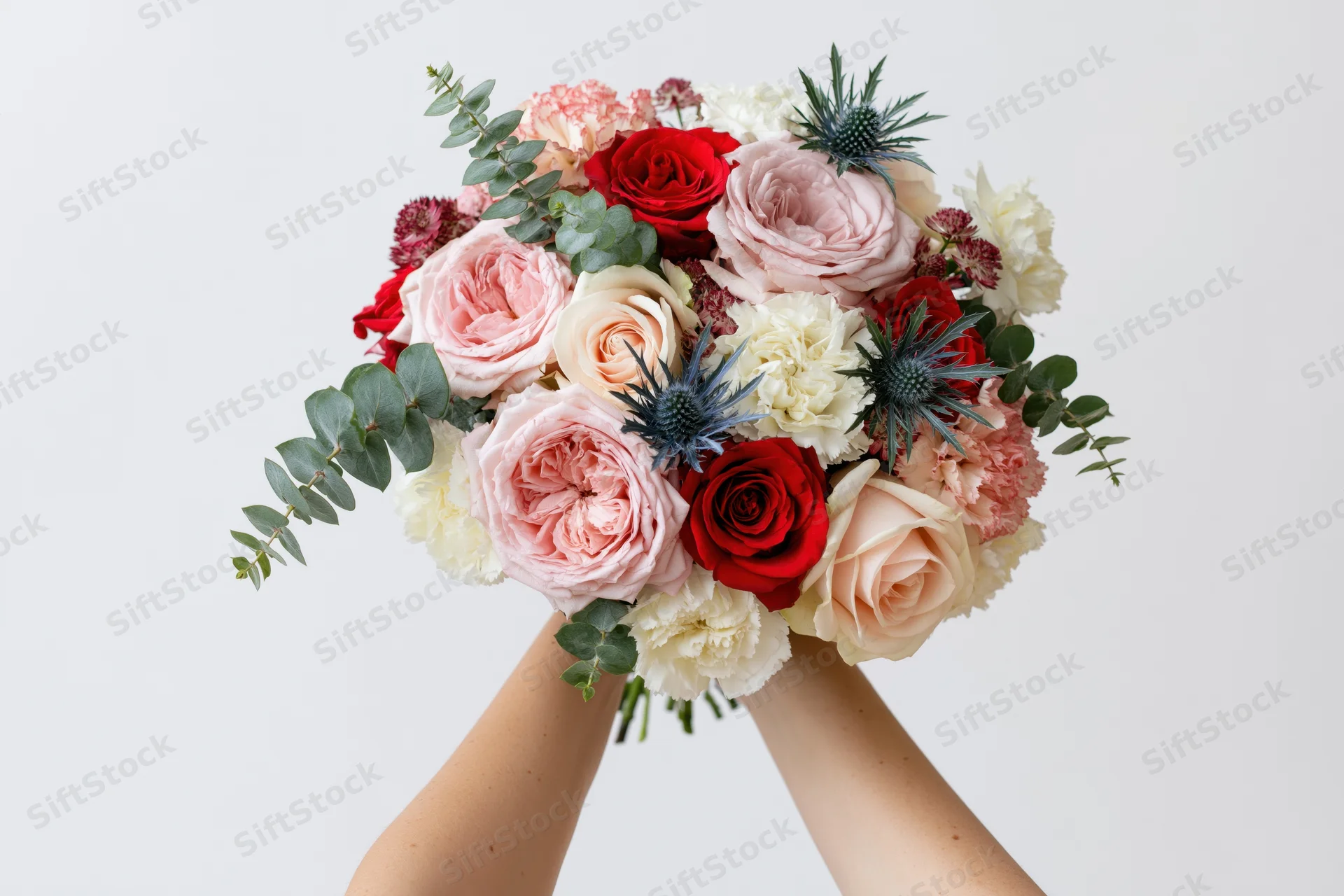 Woman holding lush mixed flower bouquet with roses, peonies, eucalyptus and thistle against white background