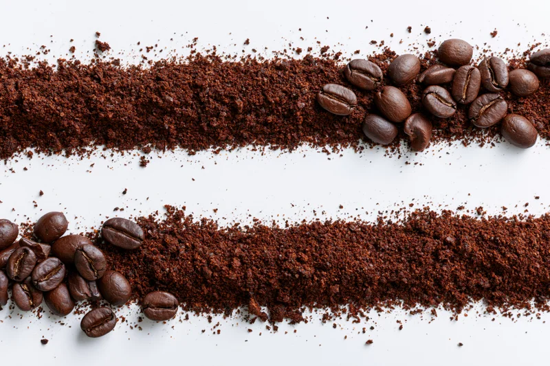 Two horizontal strips of ground coffee with whole beans scattered on white background