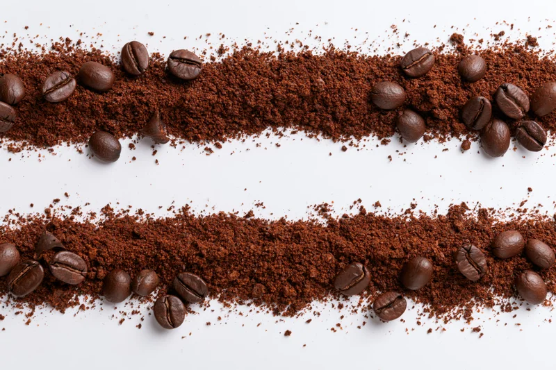 Two horizontal strips of ground coffee and whole beans scattered on white surface