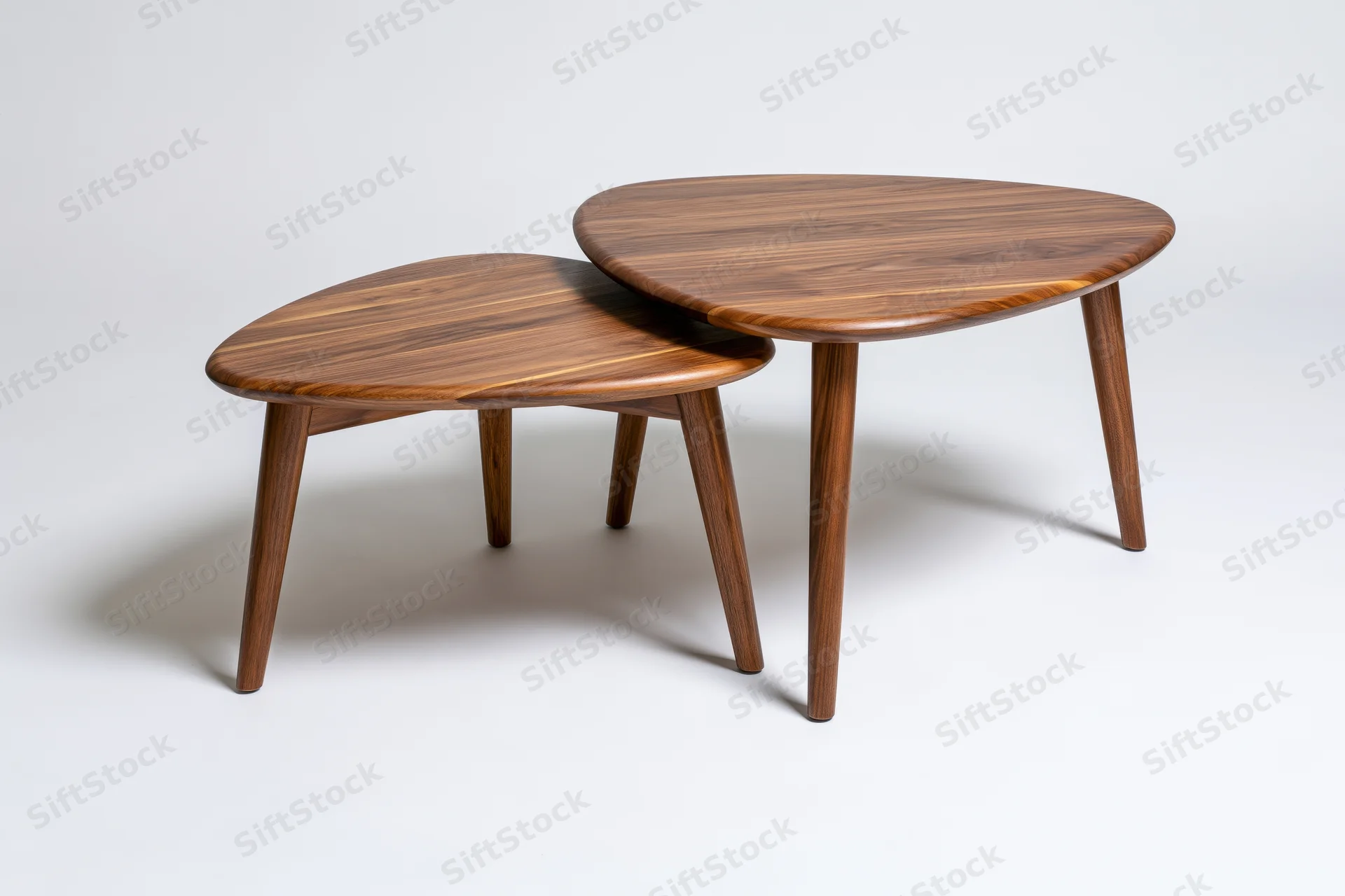 Two midcentury modern nesting coffee tables with rounded triangular tops and tapered legs on white background