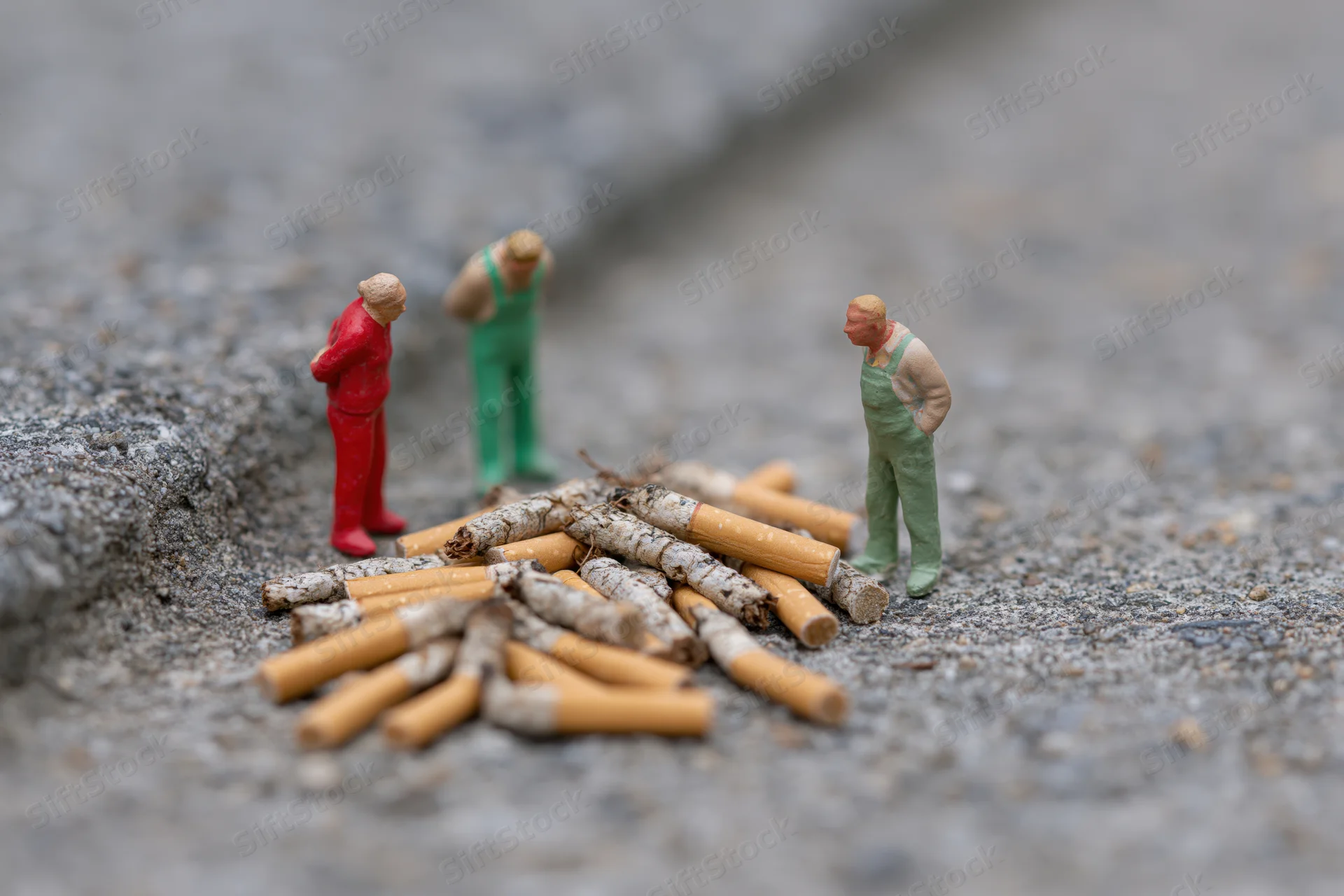 Miniature figurines standing around a pile of cigarette butts on gravel ground