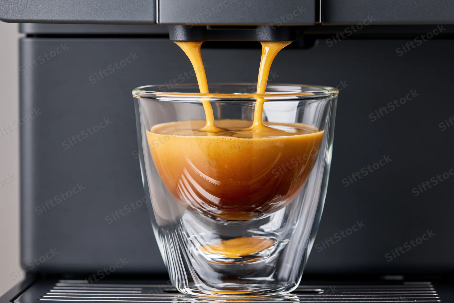 Espresso pouring from a coffee machine into a double-walled glass cup on a drip tray