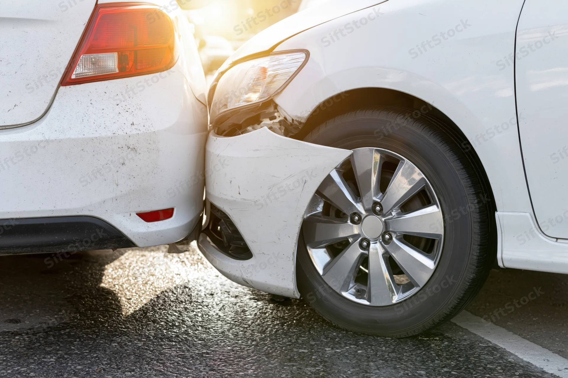 Two white cars in rear-end collision showing damaged front bumper and rear end on asphalt parking lot