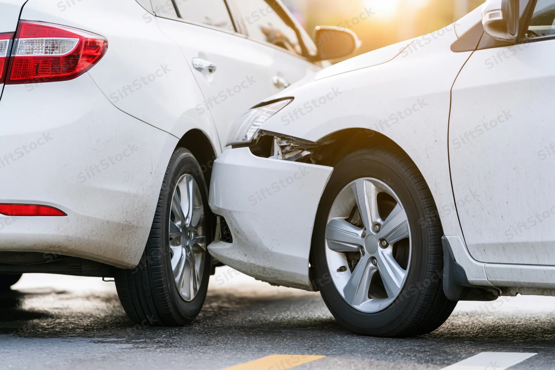 Two white cars in rear-end collision showing damaged front bumper and rear end on asphalt road