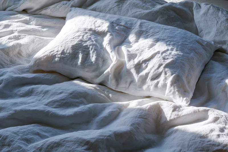 Crumpled white linen pillow resting on rumpled duvet in unmade bed