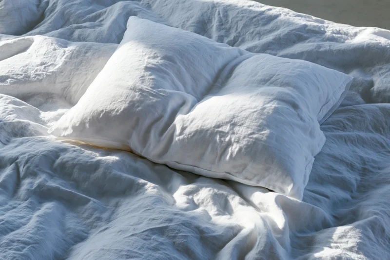 Unmade bed with crumpled white linen pillow and rumpled duvet in natural daylight