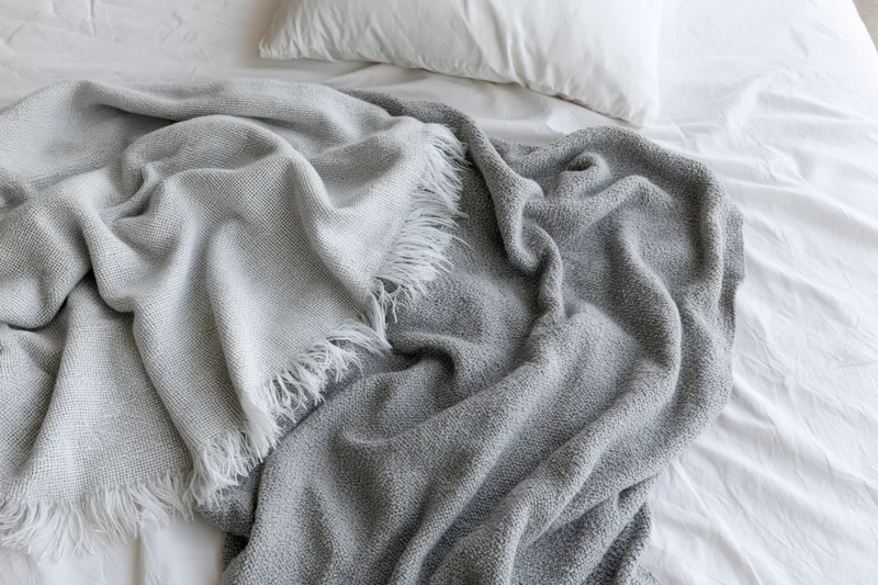 Unmade bed with two gray throws casually draped and rumpled on white sheets