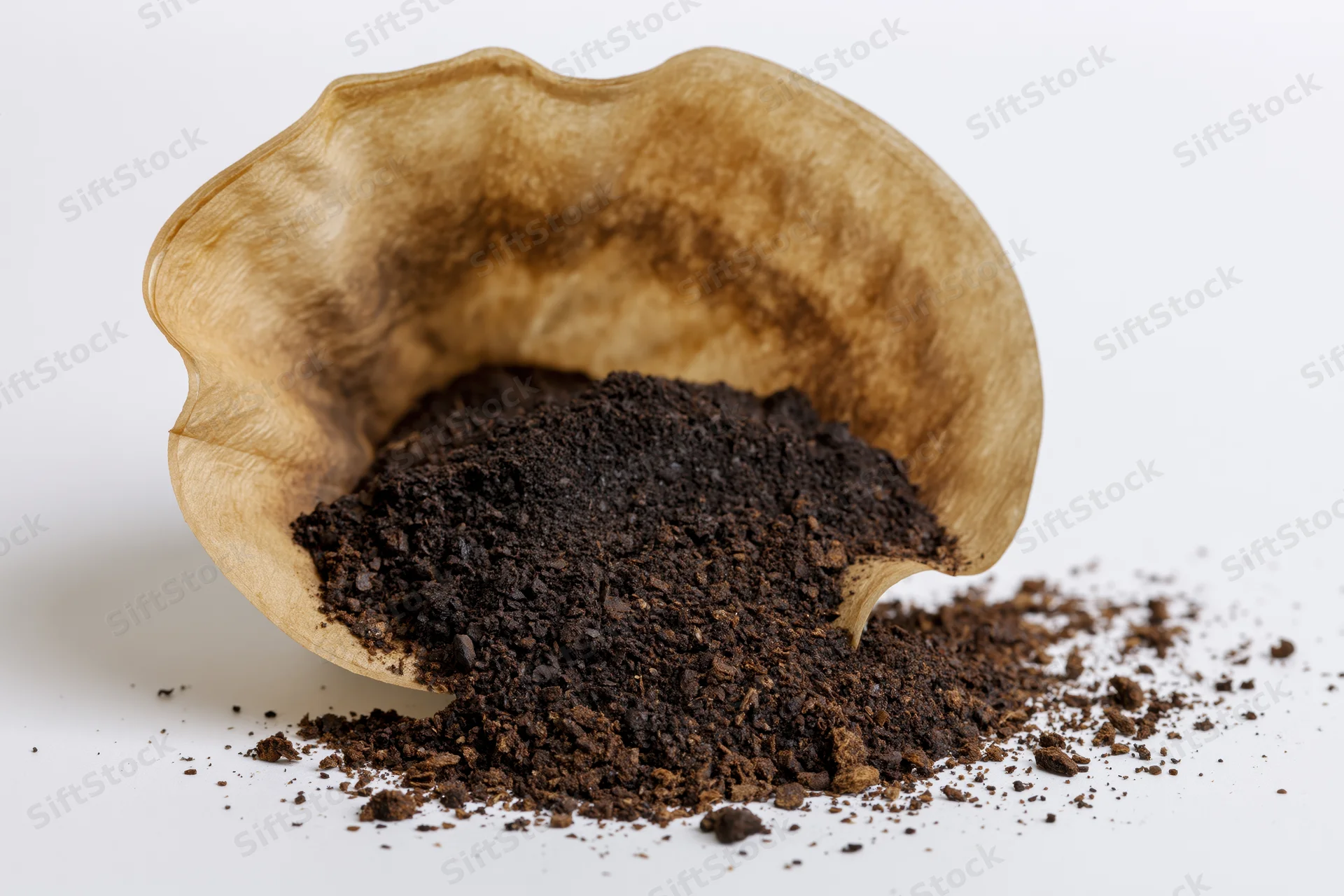 Used paper coffee filter tipped over with dark coffee grounds spilling onto white surface