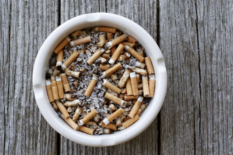 White ceramic ashtray filled with used cigarette butts and ash on a weathered wooden surface