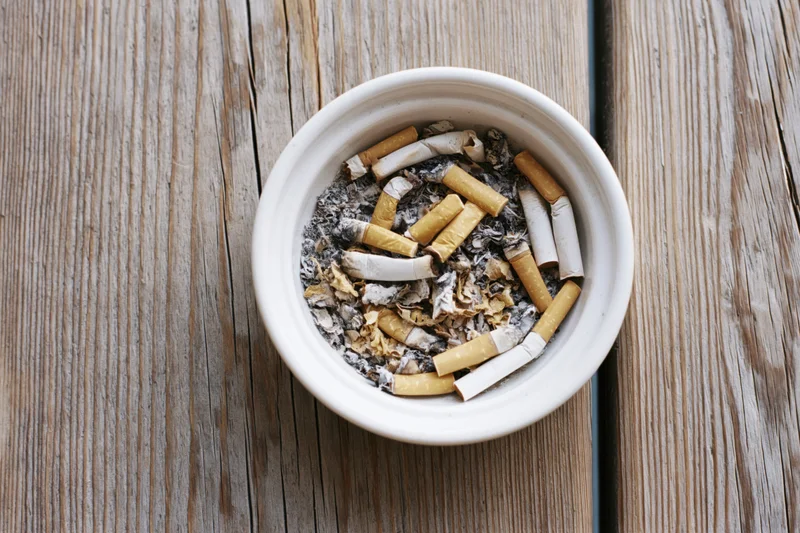 White ceramic ashtray filled with cigarette butts and ash on a wooden table