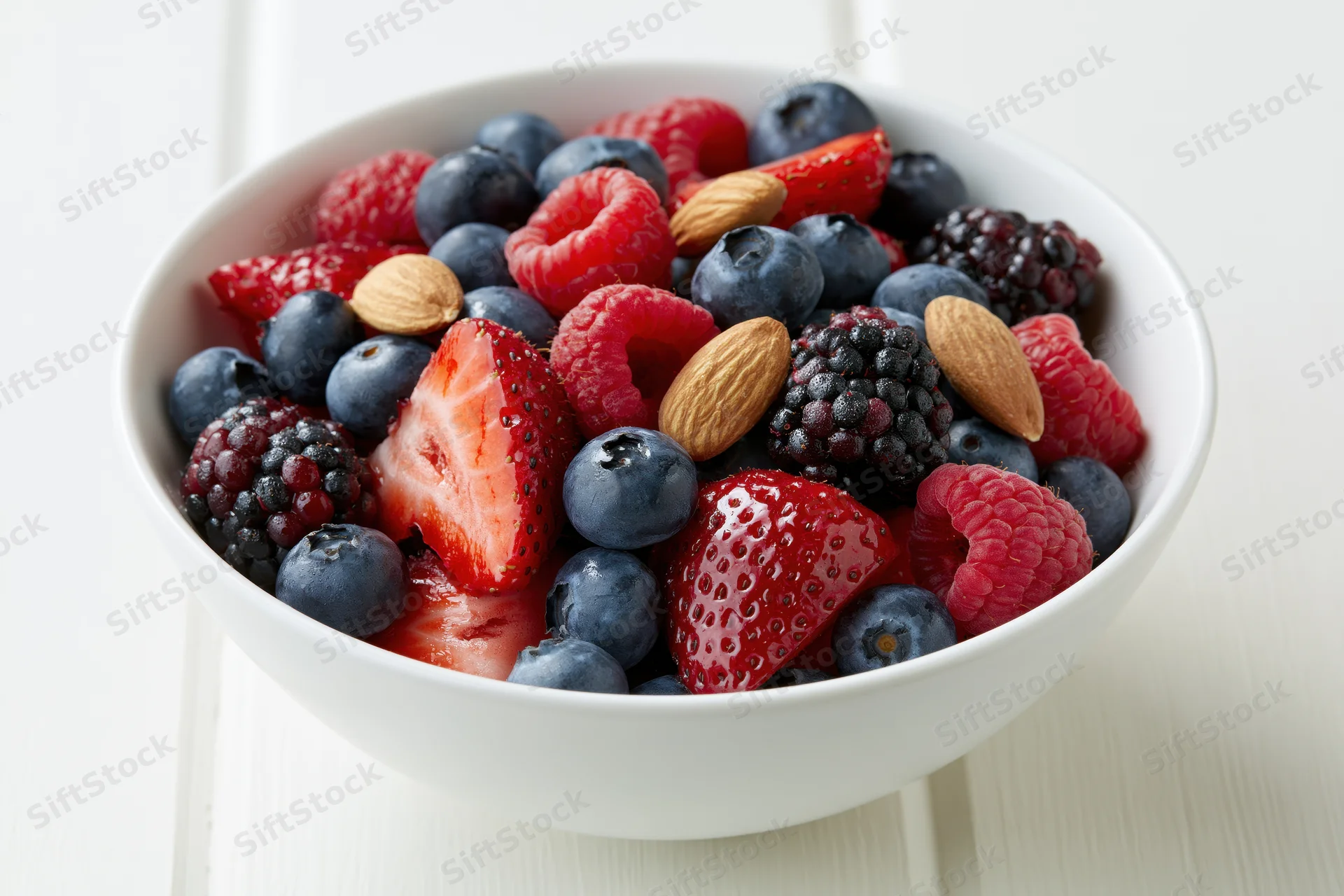 A white ceramic bowl filled with mixed berries and almonds on a light wooden surface