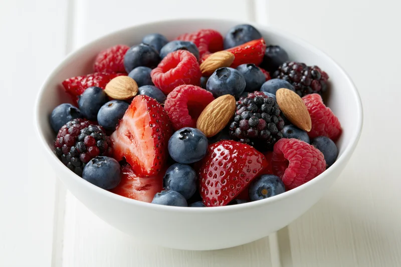 A white ceramic bowl filled with mixed berries and almonds on a light wooden surface