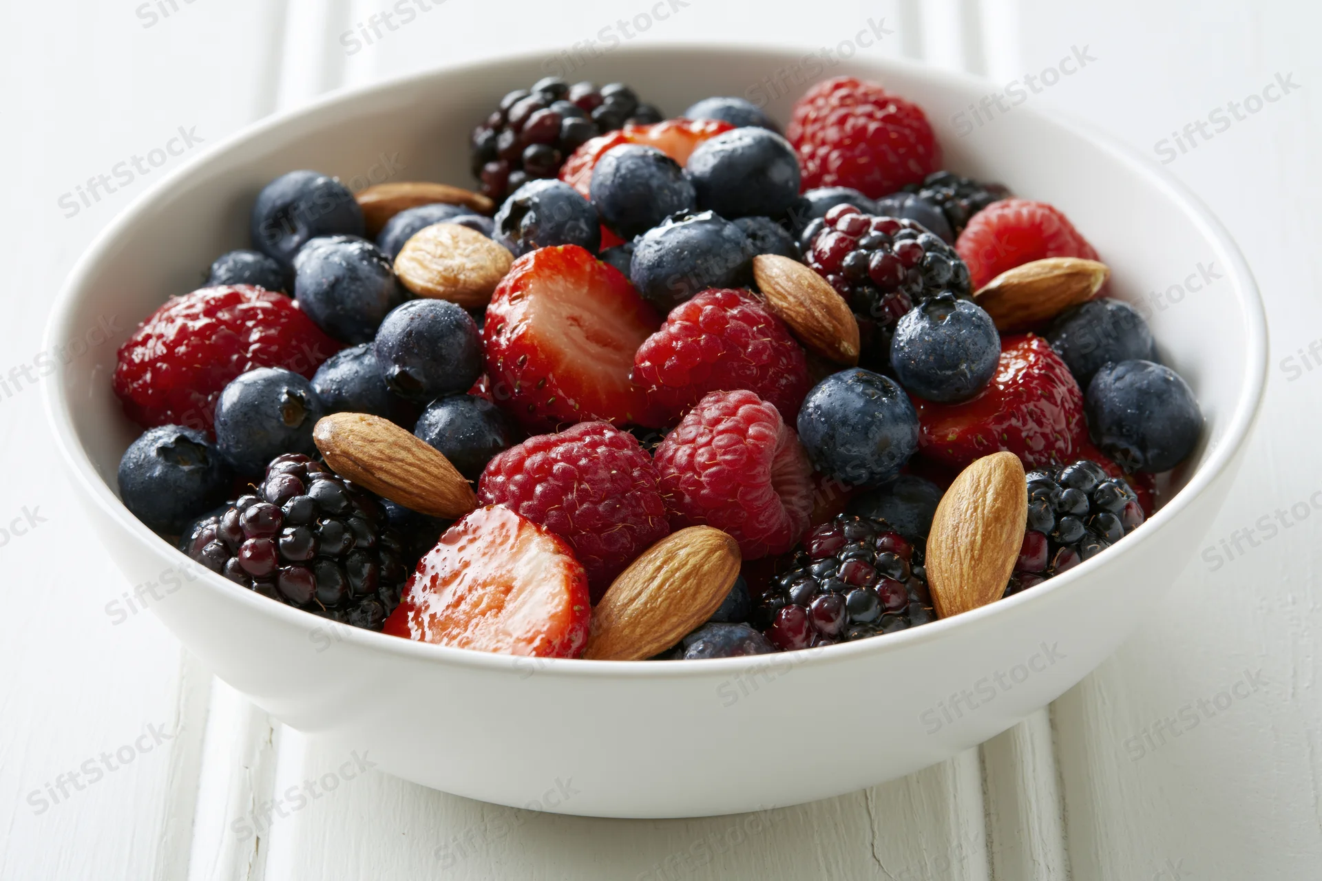 White ceramic bowl filled with mixed berries and almonds on wooden surface