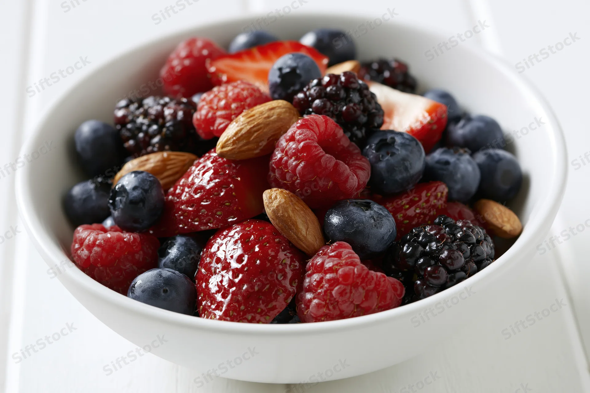 White ceramic bowl filled with mixed berries and almonds on a light surface