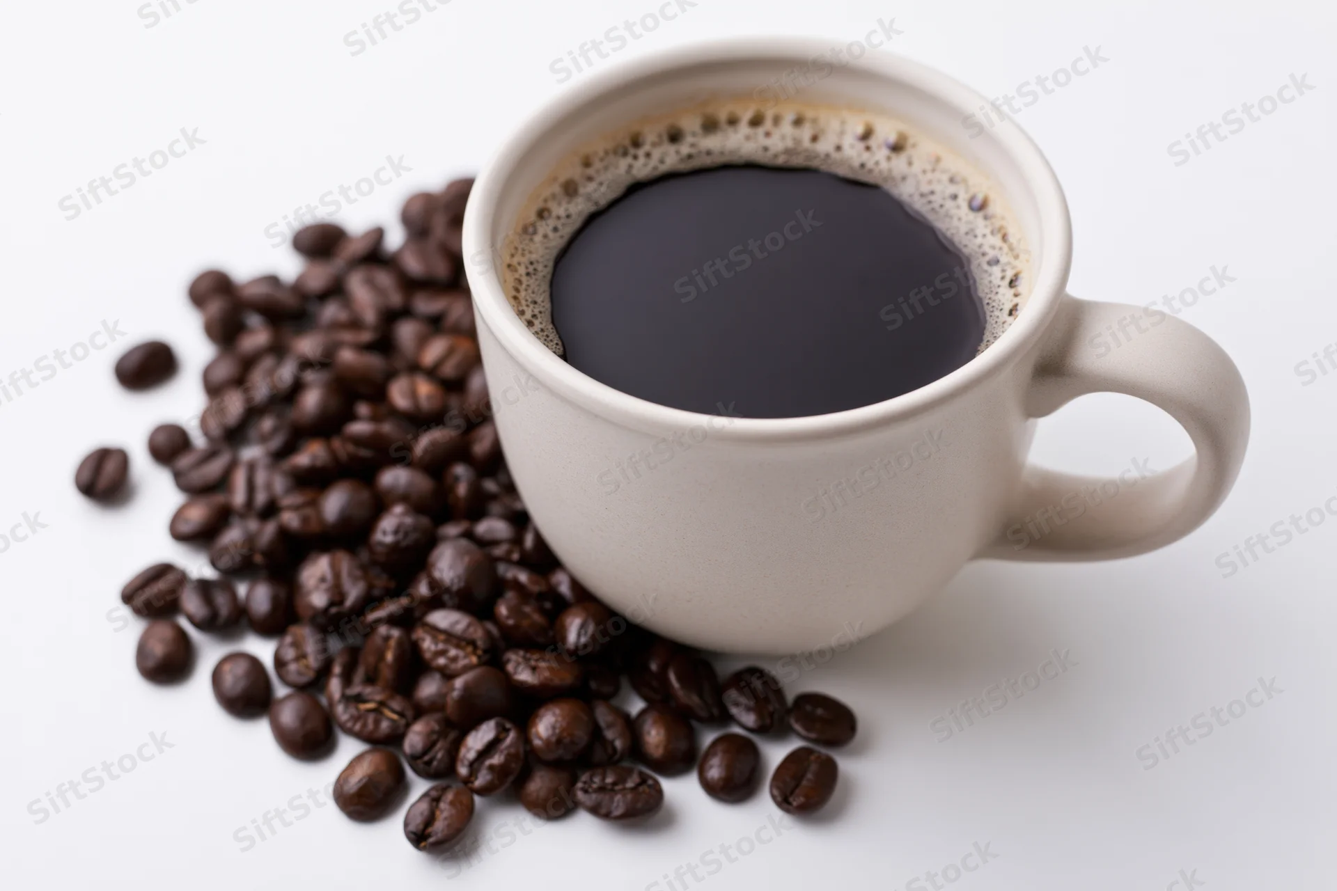 White ceramic cup filled with black coffee and foam beside scattered coffee beans on white surface