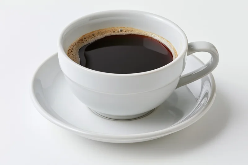 White ceramic coffee cup filled with black coffee on a saucer against a plain white background