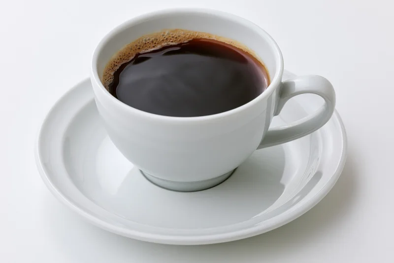White ceramic coffee cup filled with black coffee on saucer against plain white background
