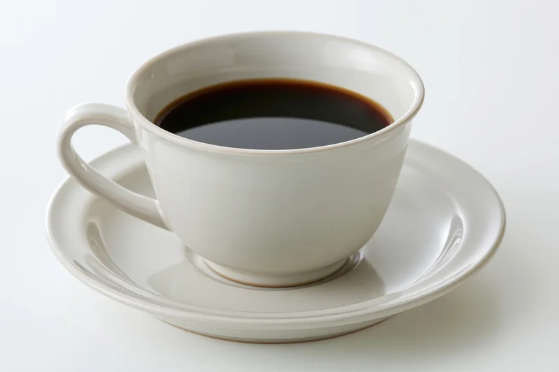 White ceramic coffee cup filled with black coffee on a matching saucer against a plain white background