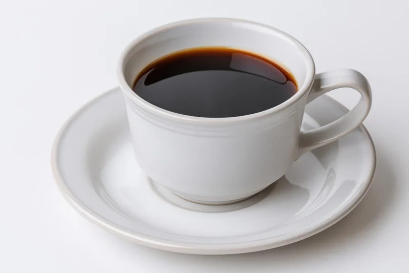 White ceramic coffee cup filled with black coffee on a matching saucer against a plain white background