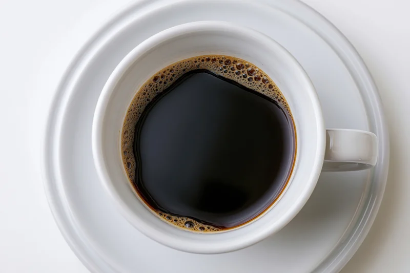 Overhead view of a white ceramic coffee cup filled with black coffee on a saucer