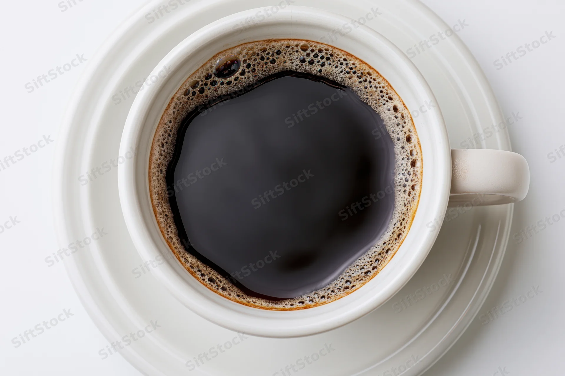 Overhead view of a white ceramic coffee cup filled with black coffee and foam on a saucer