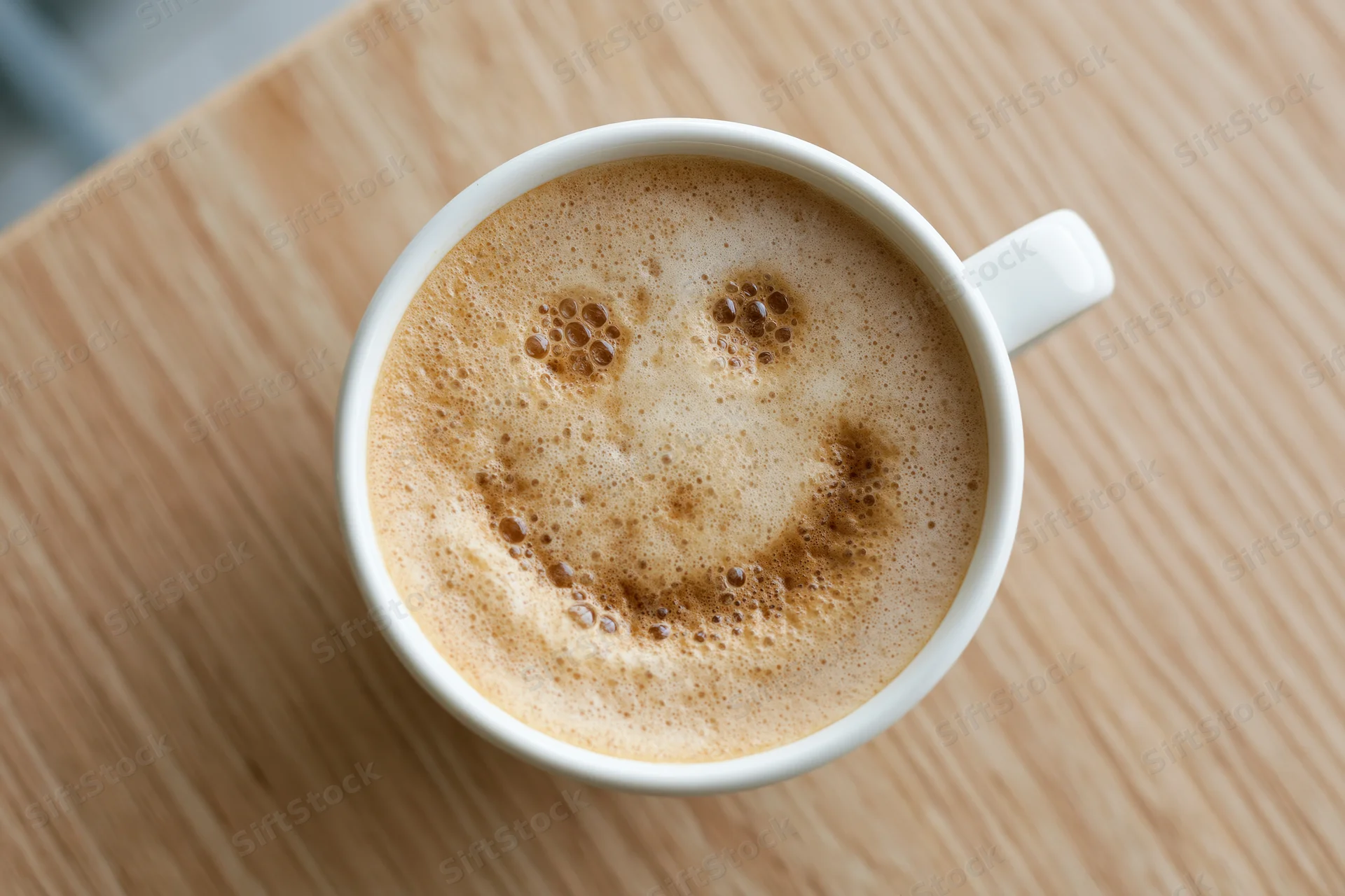 White ceramic coffee cup with smile-shaped foam on wooden table