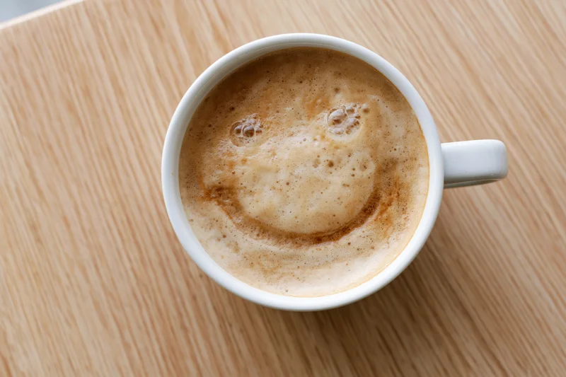 White ceramic coffee cup with smile-shaped foam on wooden table, top view