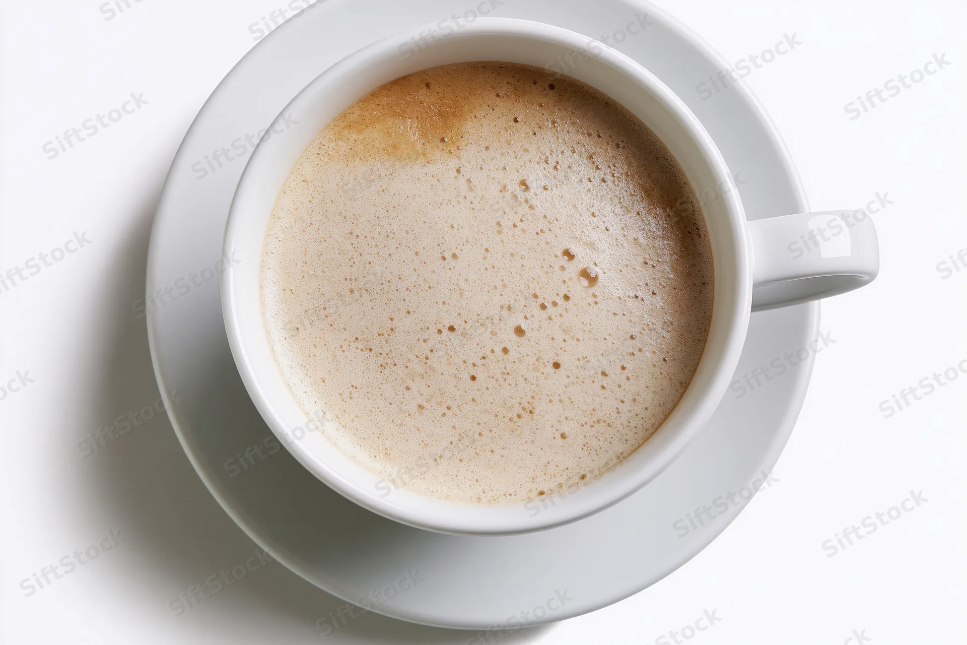 White ceramic coffee cup filled with frothy beverage on matching saucer, overhead view