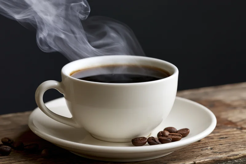 Steaming coffee cup on a saucer with scattered beans on a wooden table