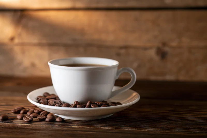 White ceramic coffee cup on saucer with roasted coffee beans on wooden table