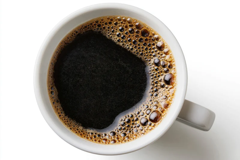 Overhead view of a white ceramic mug filled with black coffee and foam on a plain white surface