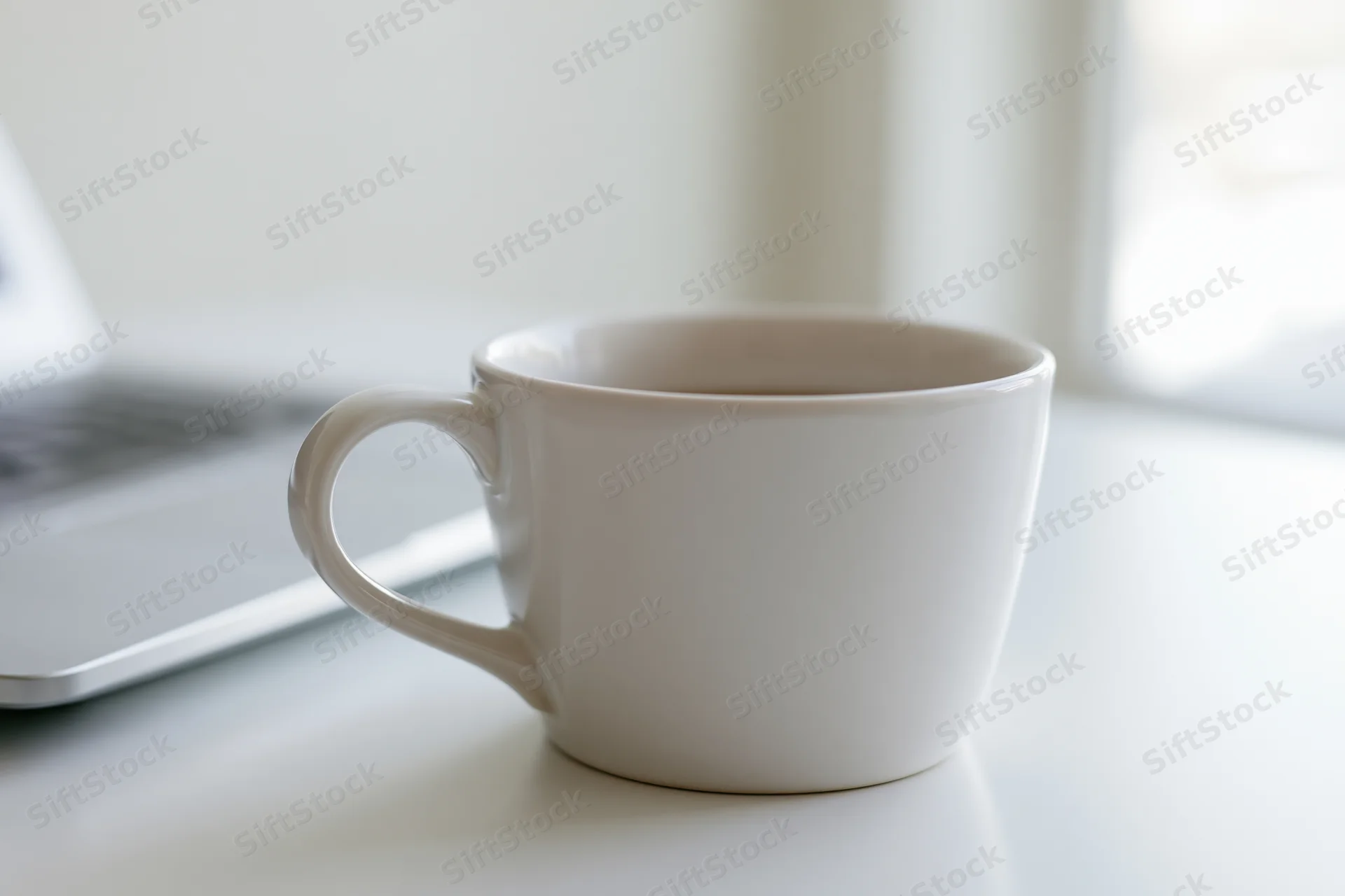 White ceramic coffee mug on a white desk beside a laptop in a bright indoor workspace