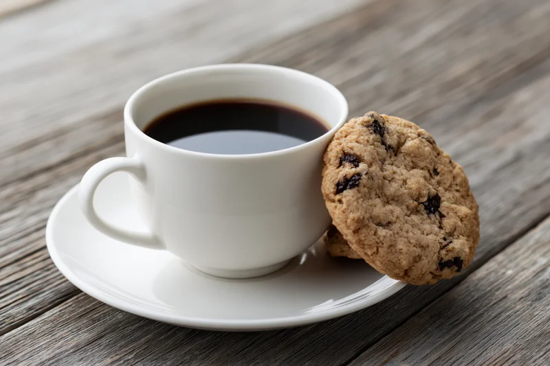 White ceramic coffee cup with chocolate chip cookie on wooden table