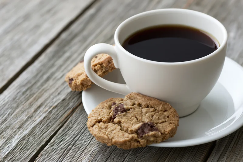 White ceramic cup of black coffee with chocolate chip cookies on a wooden table